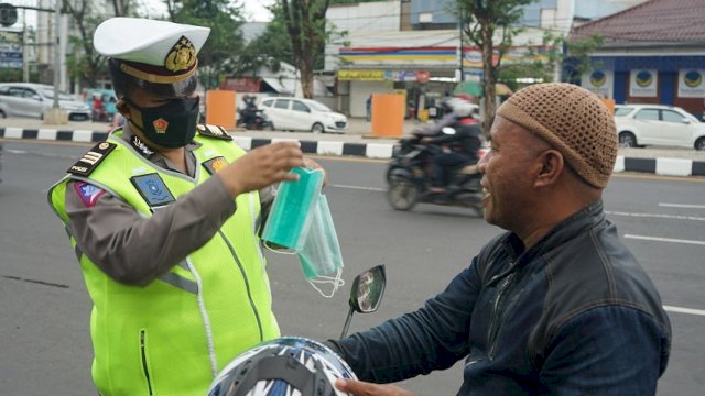 Seorang polantas sedang memberikan masker kepada pengendara di Jalan AP Pettarani Makassar
